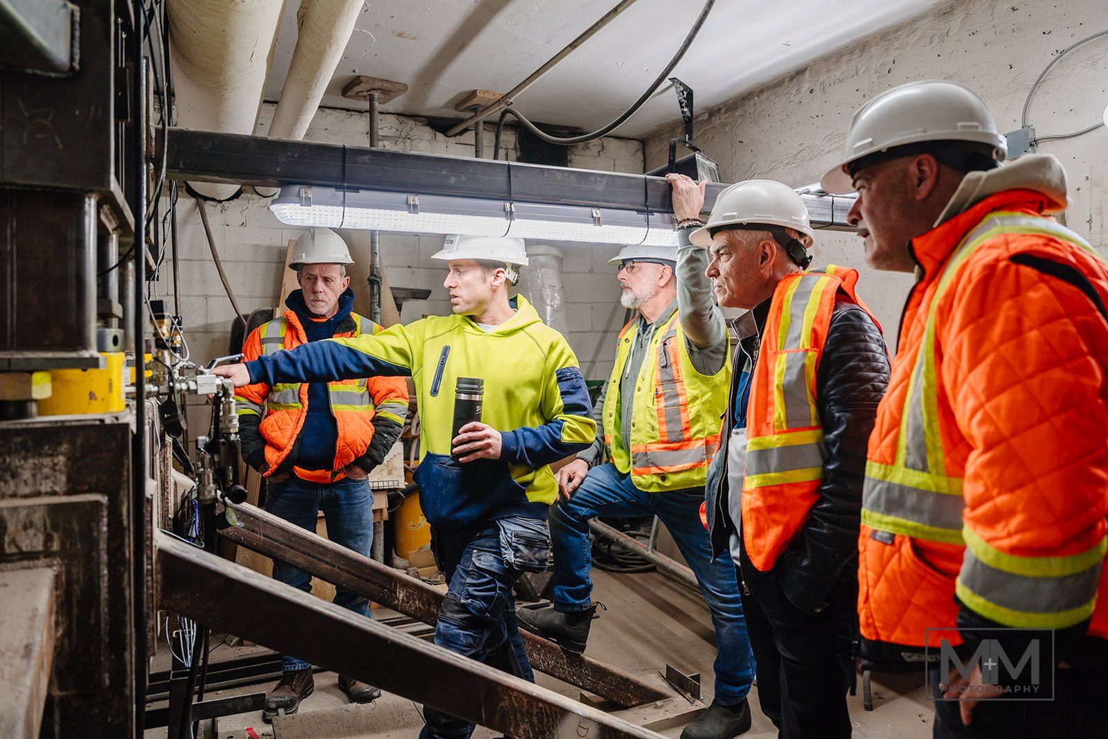 Engineers and contractors in hard hats gathered at the bracket assembly, one pointing at a load point
