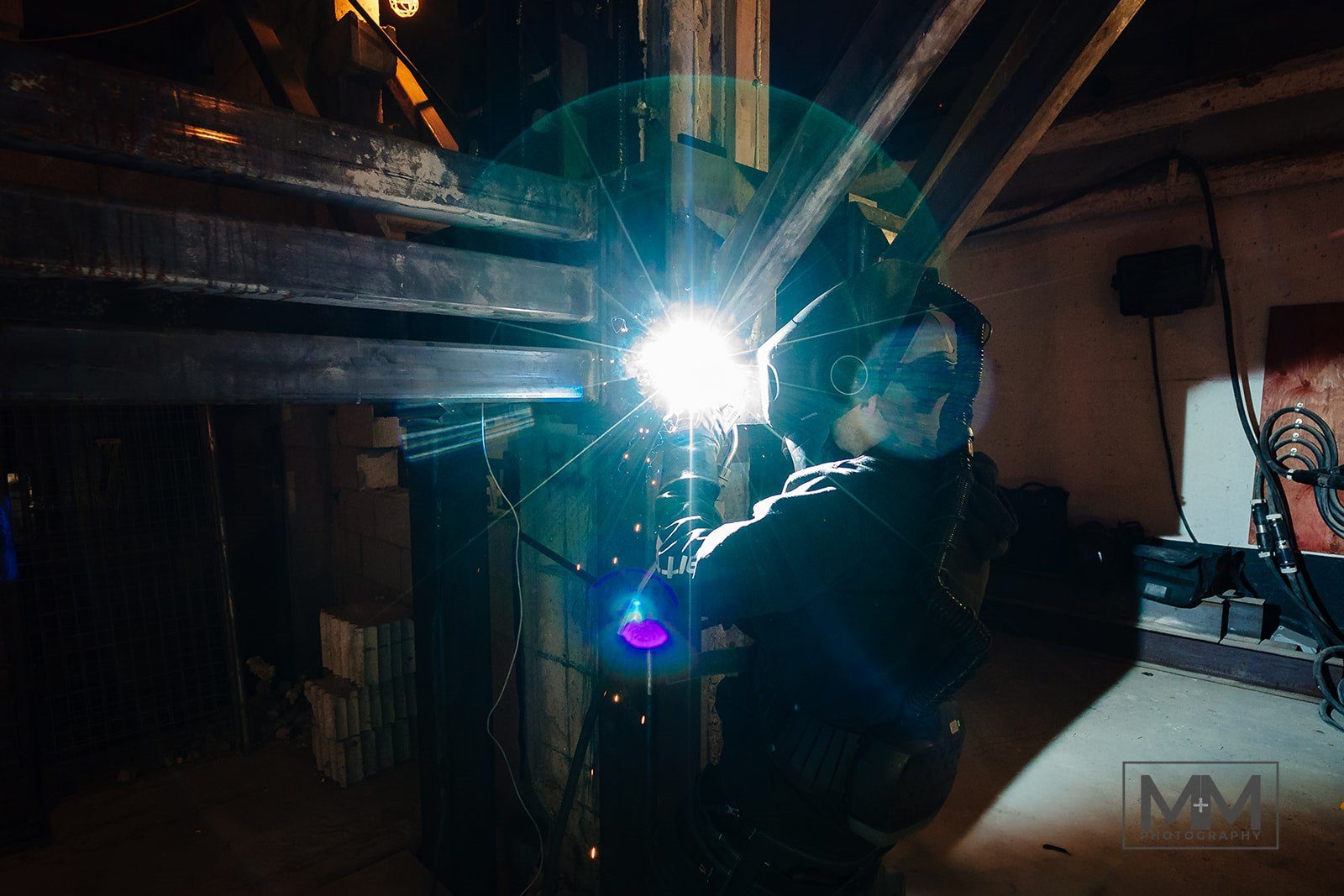A welder working on reinforcing steel inside the steel bracket assembly, lit by the arc