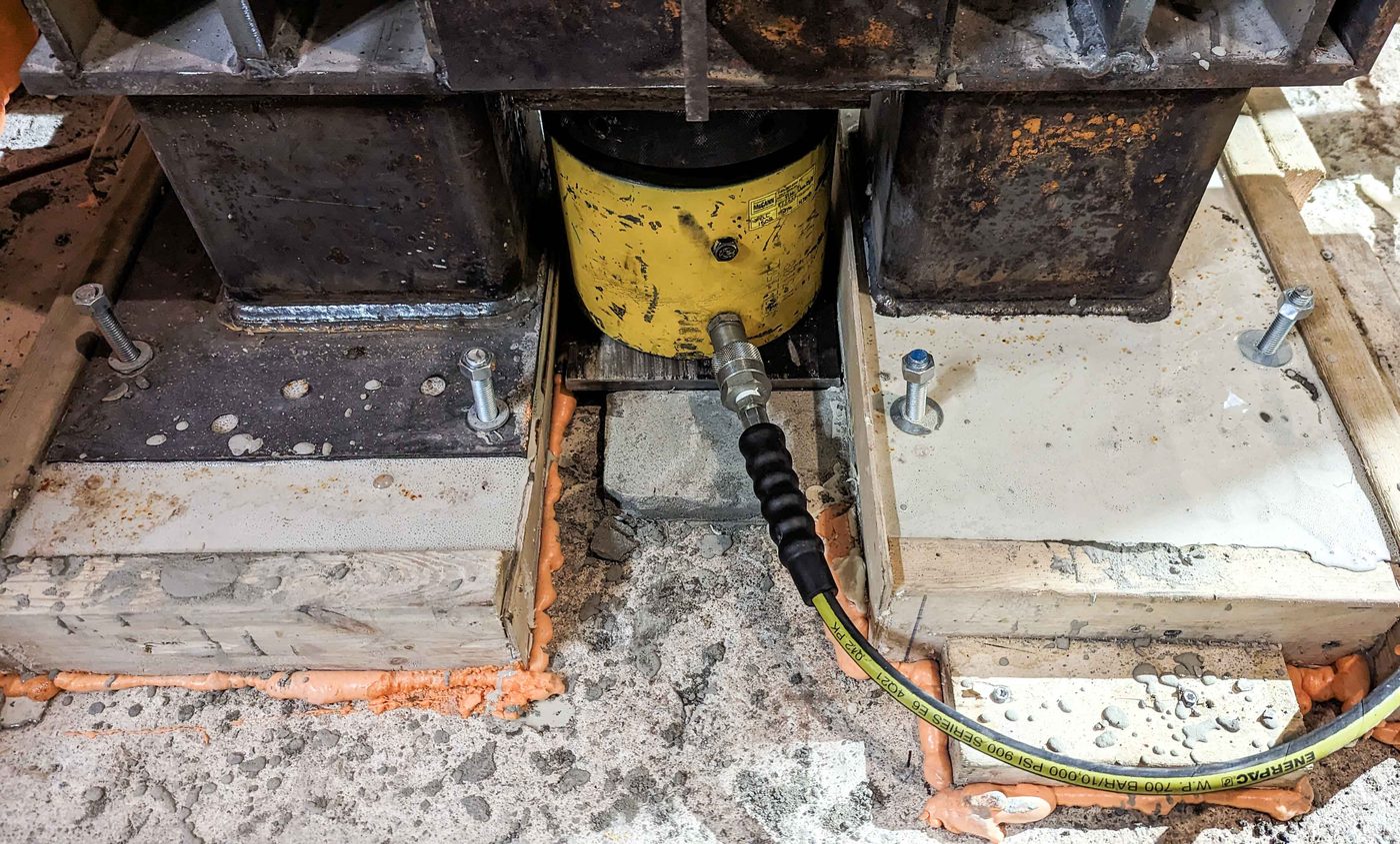 Yellow hydraulic cylinder set between two anchored steel post bases