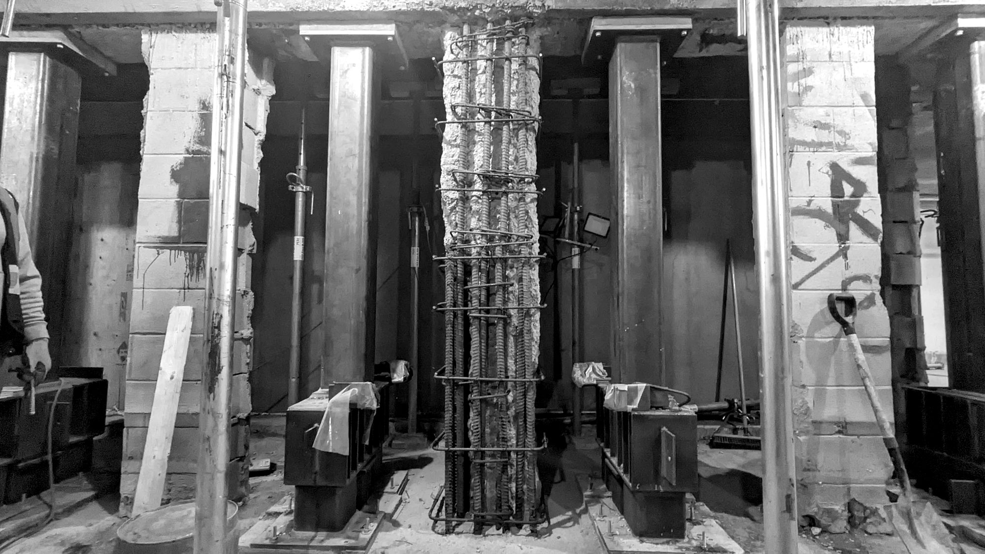 Damaged column stripped to its reinforcing cage, standing between two steel shoring posts on anchored bases